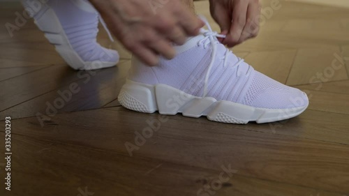 Close up of sporty senior man tying shoelaces on sneaker. Home workout.