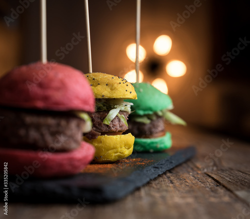 Mini hamburger colorati di manzo su piatto di ardesia, tavolo in legno e background con luce calda