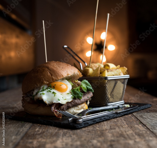 American hamburger con uovo, patatine, insalata servito su piatto di ardesia, tavolo in legno e background con luce calda