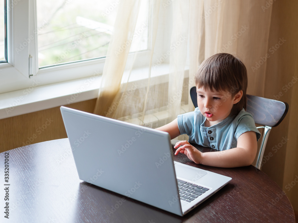 Curious toddler boy explores the laptop and presses buttons on computer keyboard. Online education for babies. Curious toddler boy explores the laptop and presses buttons on computer keyboard. Online education for babies.