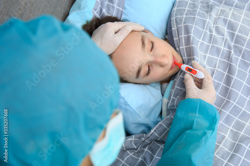 Mother measuring temperature of her ill kid. Sick child with high fever laying in bed and mother holding thermometer. Children and illness COVID-2019 disease concept. Home quarantine at Coronavirus