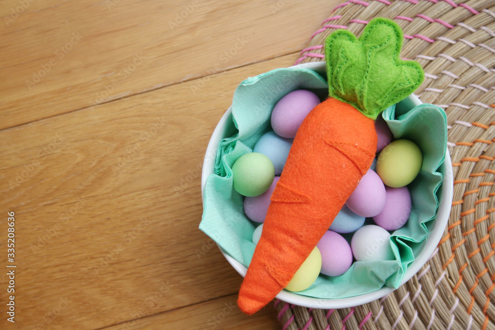 Carrot made by felt with on a bowl full of colorful sugar Easter eggs on wooden table. Easter background
Carrot made by felt with on a bowl full of colorful sugar Easter eggs on wooden table. Easter background
