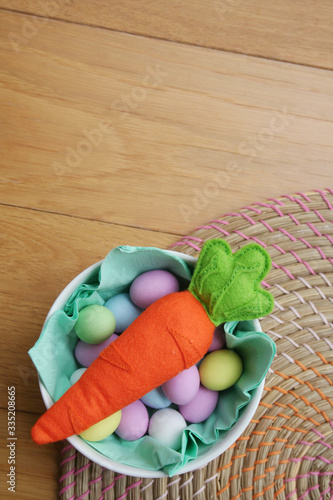 Carrot made by felt with on a bowl full of colorful sugar Easter eggs on wooden table. Easter background 