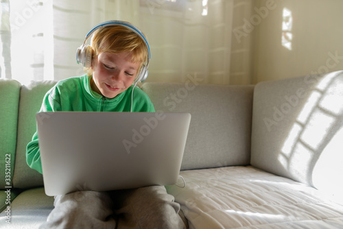 Happy young handsome boy with headphones using laptop at home