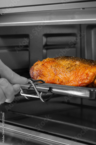 Man taking a leg of lamb joint out of an electric oven grill. With selective colour
