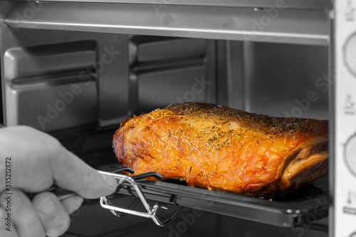 Man taking a leg of lamb joint out of an electric oven grill. With selective colour