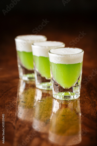 fresh sweet green sour shot alcohol cocktails on the dark wooden background, side view, vertical