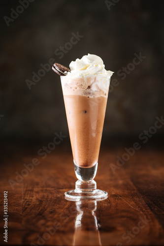 delicious cold chocolate ice cream milkshake with cookie in a long glass, dark wooden background, side view, vertical