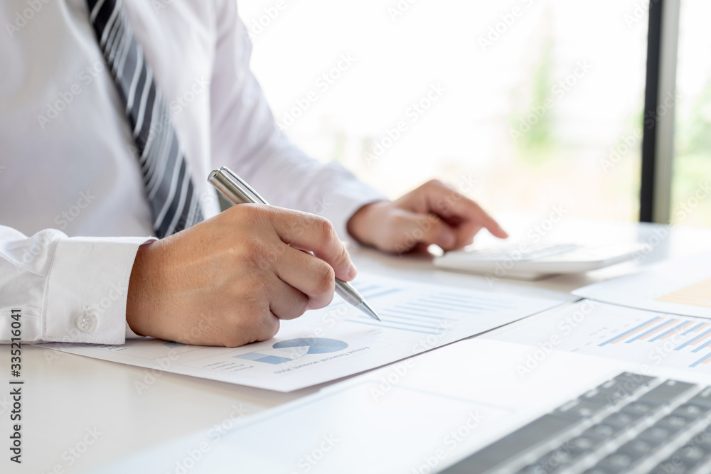 A business man is sitting at a desk and calculating financial graphs about real estate investment expenditures A business man is sitting at a desk and calculating financial graphs about real estate investment expenditures