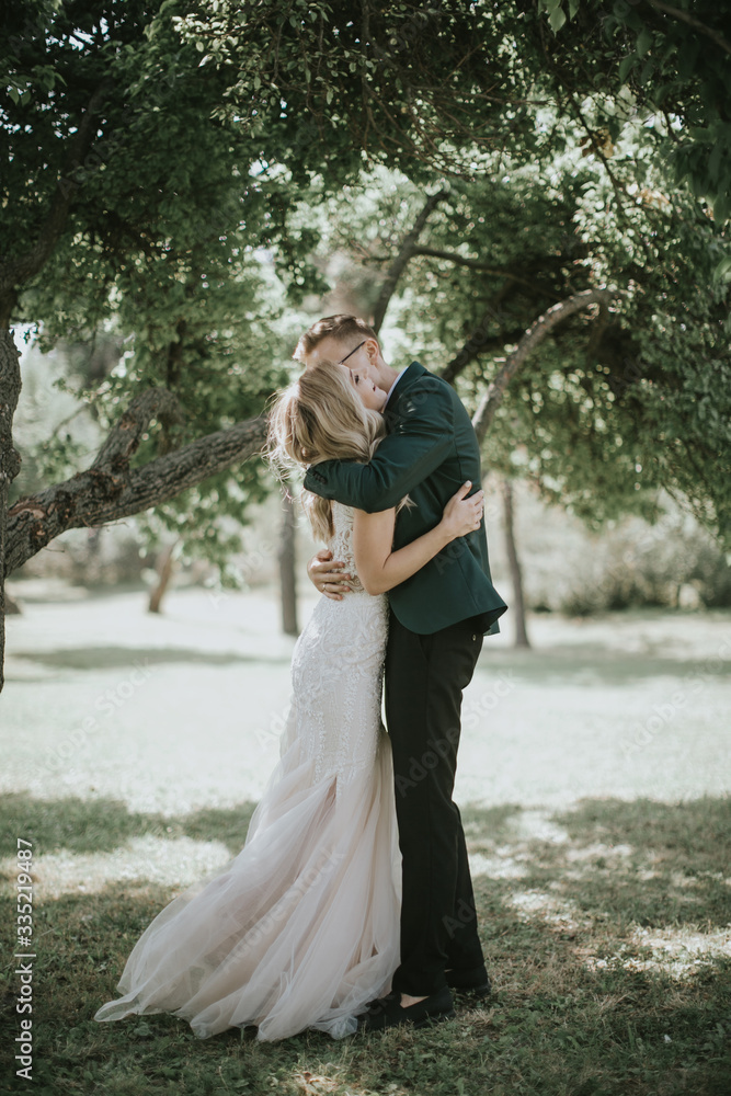 Portrait of a lovely bride and groom embrace, kiss and hug each other. Couple in love in the bosom of nature . Handsome groom and beautiful blonde bride posing in the forest. Modern dress and suit