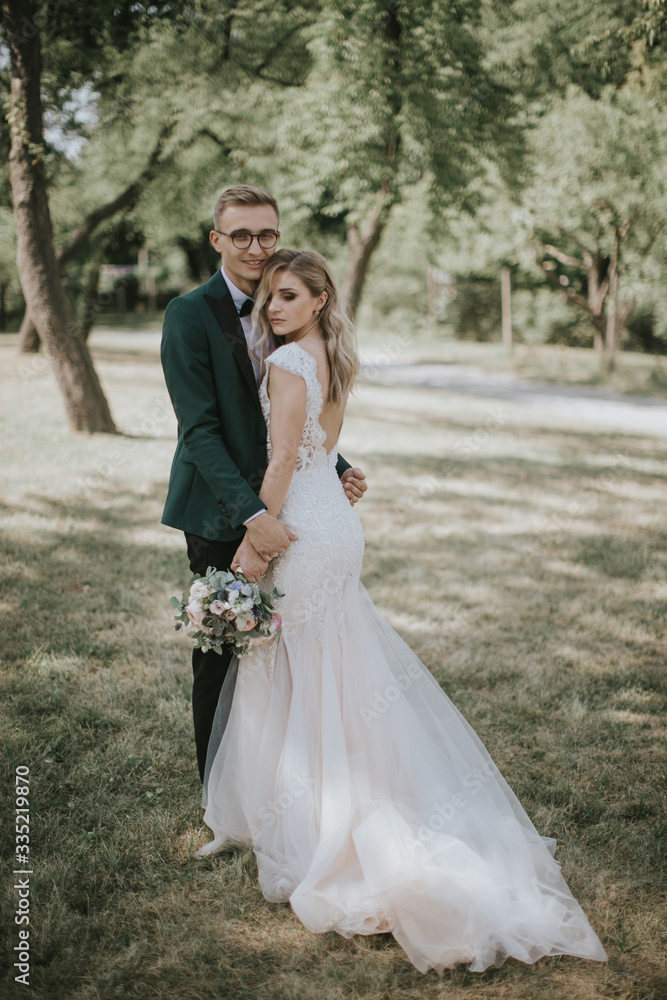 Portrait of a lovely bride and groom embrace, kiss and hug each other. Couple in love in the bosom of nature . Handsome groom and beautiful blonde bride posing in the forest. Modern dress and suit