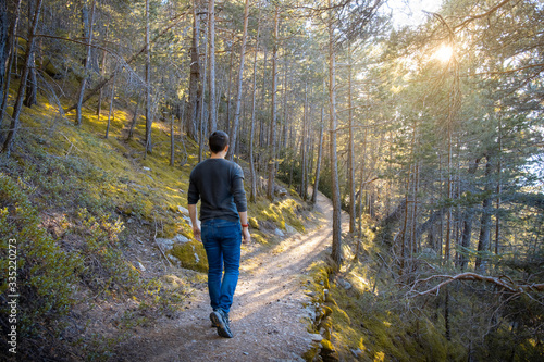 Young man seen from the back walking through the mountain in jeans and a ray of sunshine through the trees.
