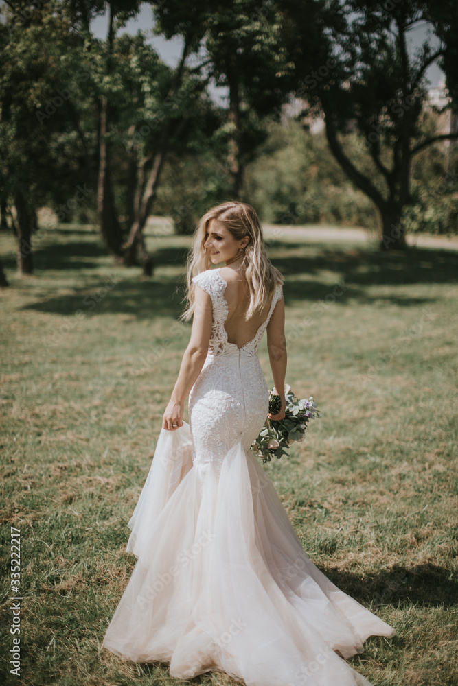 Portrait of a wedding bride walking in a white modern hipster dress. Caucasian blonde bride in a vintage dress in the forest on sunset. Attractive lady posing with a bouquet of flowers