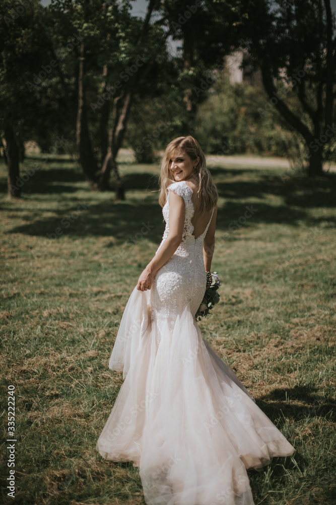 Portrait of a wedding bride walking in a white modern hipster dress. Caucasian blonde bride in a vintage dress in the forest on sunset. Attractive lady posing with a bouquet of flowers Portrait of a wedding bride walking in a white modern hipster dress. Caucasian blonde bride in a vintage dress in the forest on sunset. Attractive lady posing with a bouquet of flowers