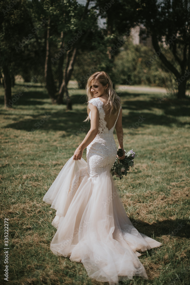 Portrait of a wedding bride walking in a white modern hipster dress. Caucasian blonde bride in a vintage dress in the forest on sunset. Attractive lady posing with a bouquet of flowers