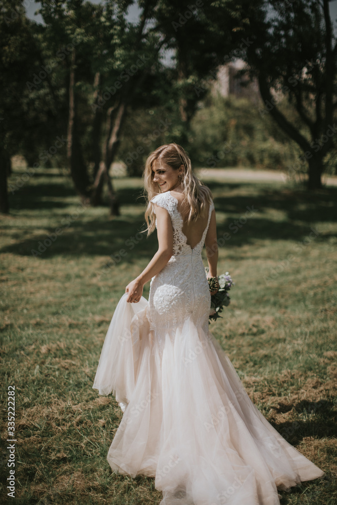 Portrait of a wedding bride walking in a white modern hipster dress. Caucasian blonde bride in a vintage dress in the forest on sunset. Attractive lady posing with a bouquet of flowers Portrait of a wedding bride walking in a white modern hipster dress. Caucasian blonde bride in a vintage dress in the forest on sunset. Attractive lady posing with a bouquet of flowers