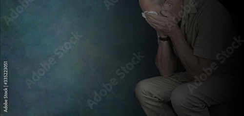 Mental Illness can be a dark place Awareness Campaign for Men background - crying man with hands holding white tissue against eyes on a rustic dark grey background with copy space 