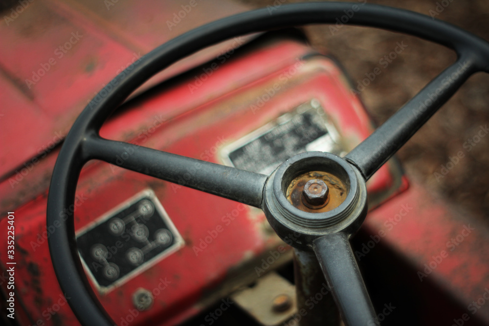 A broken red tractor in the farmland, the steering wheel is still completely placed in front of the driver's seat A broken red tractor in the farmland, the steering wheel is still completely placed in front of the driver's seat