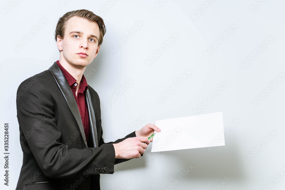 Young european business man holding A4 blank paper and points a finger at it showing data. Business background mockup, with copy space Young european business man holding A4 blank paper and points a finger at it showing data. Business background mockup, with copy space