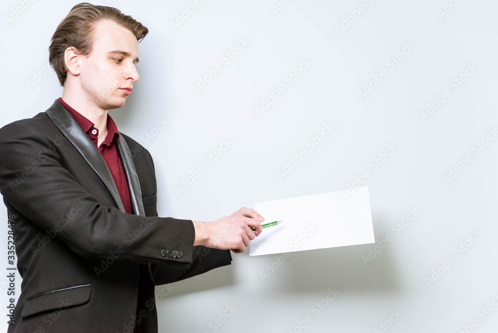 Young european business man holding A4 blank paper and points a finger at it showing data. Business background mockup, with copy space Young european business man holding A4 blank paper and points a finger at it showing data. Business background mockup, with copy space