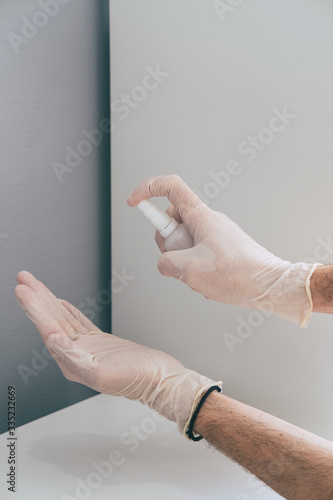 A medical worker in rubber latex gloves disinfects his hands with a sanitizer spray. Concept of protection against coronavirus