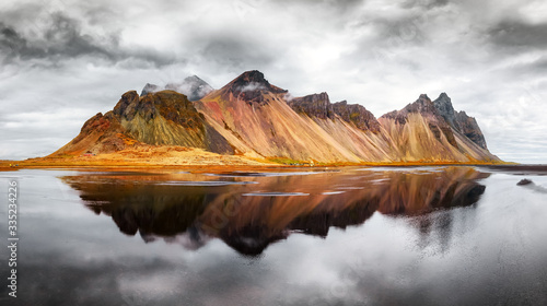 Gorgeous landscape of the famous Stokksnes mountains on Vestrahorn cape. Reflection in the clear water on the epic skies background, Iceland