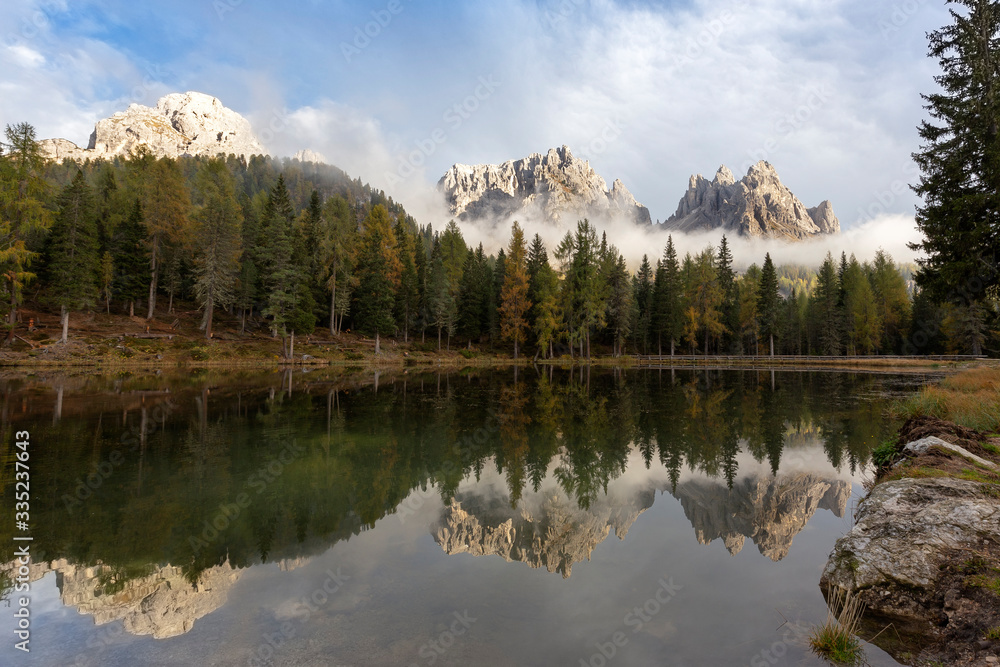 Italian Dolomites, small lake Lago d'Antorno with calm water, on the shore of high spruce. The shore of the lake frosted by morning hoarfrost. 