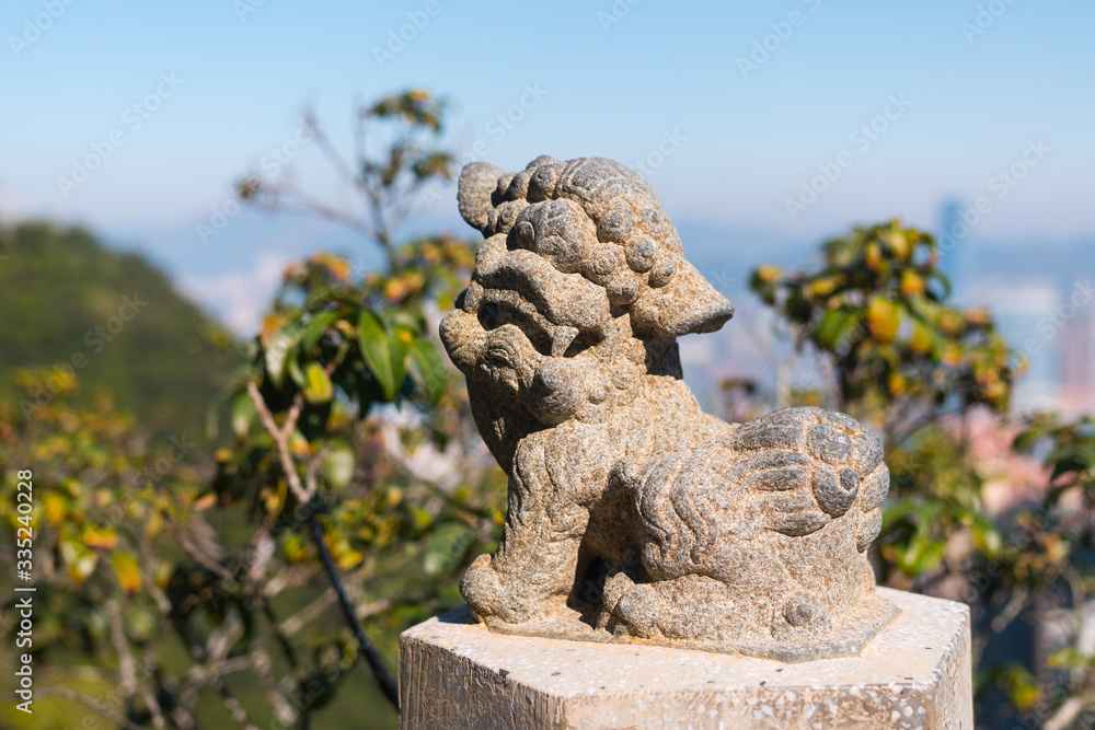 Beautiful Lion stone statue close up. Lion's Pavilion (The Peak), Hong Kong, China. Sunny day with the city's skyscrapers in the background (blurred)