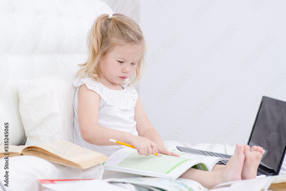 Little girl doing distance learning on a laptop at home in the bedroom. Girl doing homework lessons. Distance education during a pandemic concept Little girl doing distance learning on a laptop at home in the bedroom. Girl doing homework lessons. Distance education during a pandemic concept