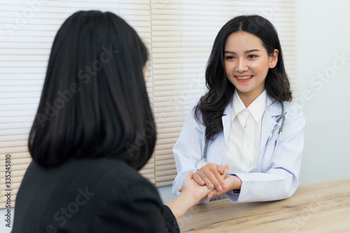 Young Asian female doctor holds adult female patient’s hand to examine and diagnose her sickness and symptom. Medicine and health care concept. Doctor and patient.