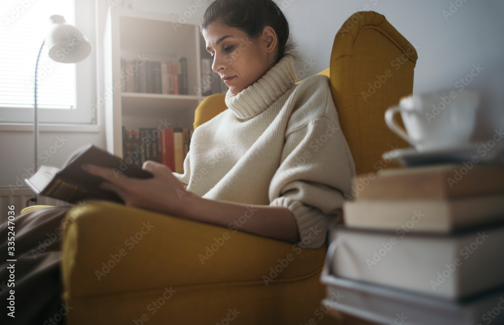 Young woman enjoy reading in armchair. Pretty girl reading stack of books Young woman enjoy reading in armchair. Pretty girl reading stack of books