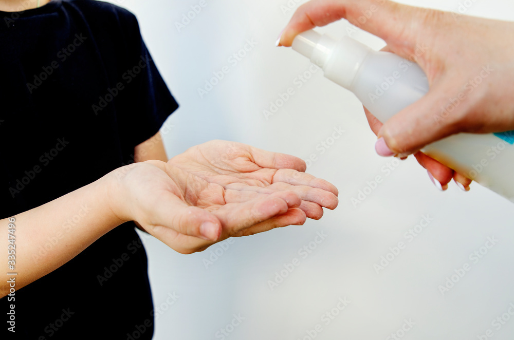 Disinfect your hands with a disinfectant and destroy the viruses on your hands. A female hand with a spray bottle with a disinfectant sprays the product on the hands of a small child. The concept of Disinfect your hands with a disinfectant and destroy the viruses on your hands. A female hand with a spray bottle with a disinfectant sprays the product on the hands of a small child. The concept of