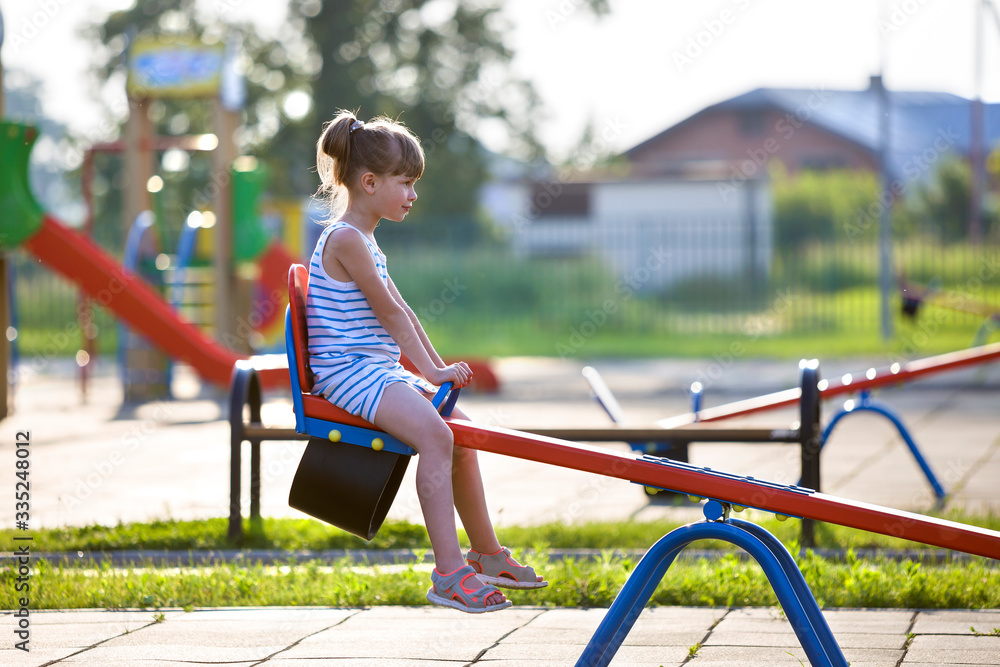 Fototapeta premium Cute young child girl outdoors on see-saw swing on sunny summer day.