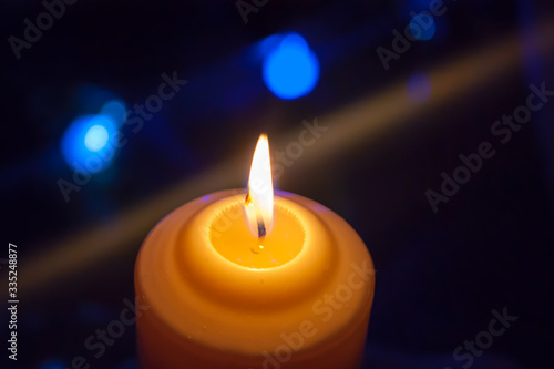 A burning orange candle on a dark background with blue lights - a Christmas New Year's eve divination mystic esoteric romance love mood. Horizontal photo, side, focus or defocus