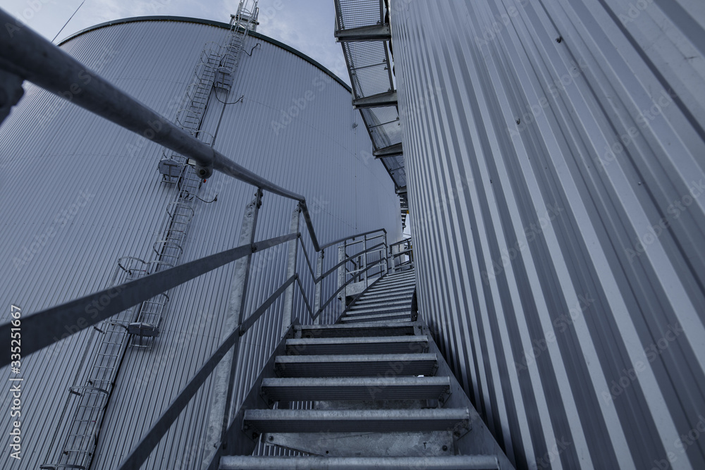 Fototapeta premium part of the metal industrial tanks outdoor. roof of technological building at the industrial plant on background. Equipment and appliances at the gas company. metal ladder stairs on the tank