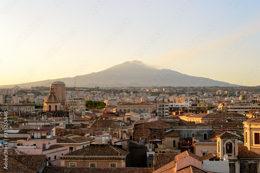 Catania, Sicily in Italy. Aerial view of the city roofs at sunset with the incredible Etna vulcano smoking in the background, nice warm colors and soft light. Shot from the badia of Sant'Agata church