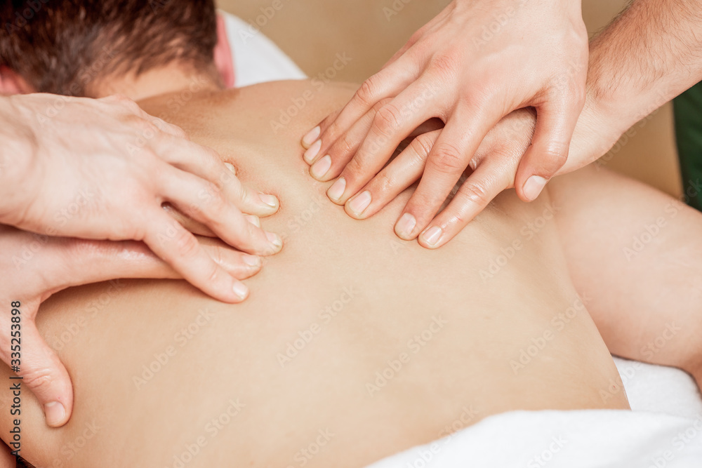 Man receiving back massage in four hands of two male therapists close up. Man receiving back massage in four hands of two male therapists close up.