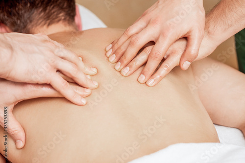 Man receiving back massage in four hands of two male therapists close up.