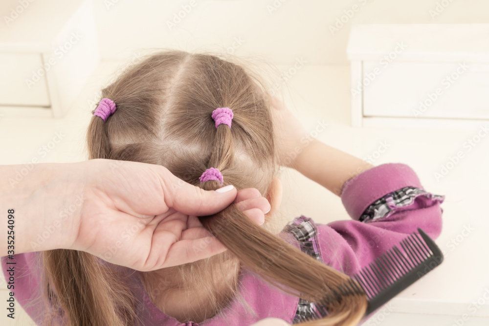 Naklejka premium hands of mother combing little smiling three year old girl