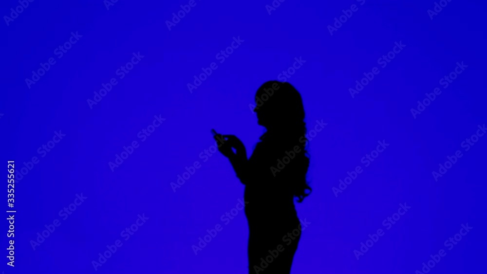 Silhouette of a young woman with curly hair talking on a cell phone on a blue background Silhouette of a young woman with curly hair talking on a cell phone on a blue background