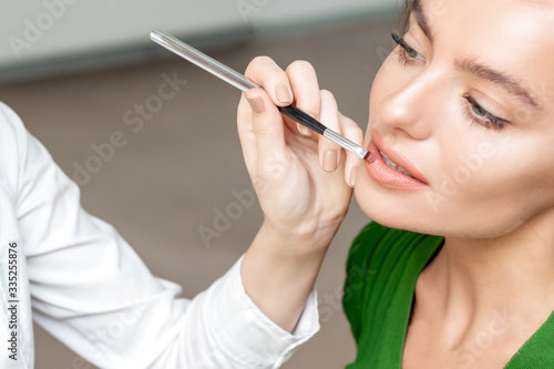 Makeup artist applies lipstick on woman lips, make up in process.