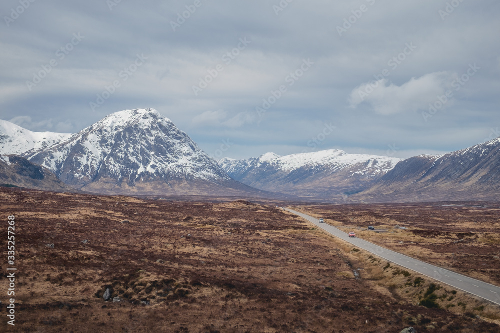 Fototapeta premium A road leading through the Scottish Highlands of Glen Coe, snowcapped mountains and valley. Scotland