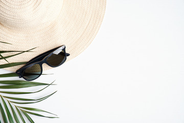 Straw hat and sunglasses with tropical palm leaf on white background. Travel or summer holiday vacation concept. Flat lay, top view, copy space