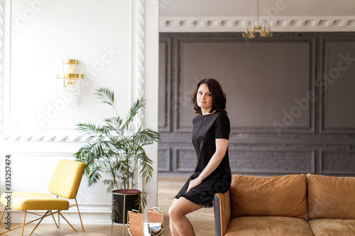 Woman in a black dress sits on the back of a sofa in the interior