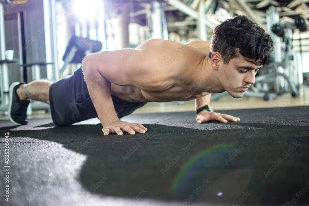 Fototapeta premium Young athletic man doing push ups in the gym