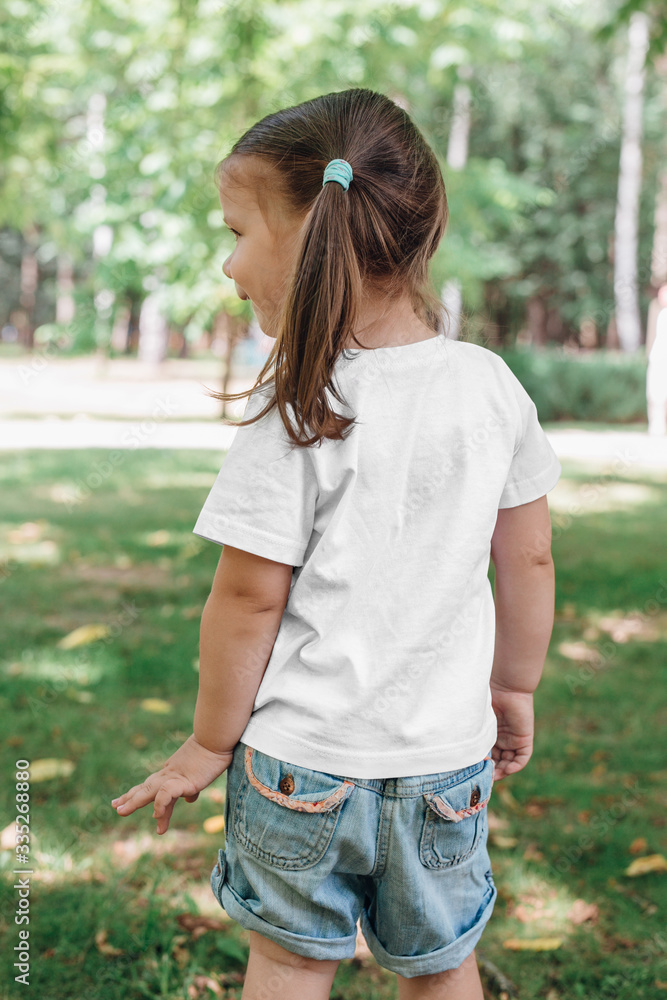 back views of little girl in blank t-shirt in park. Mockup for design back views of little girl in blank t-shirt in park. Mockup for design