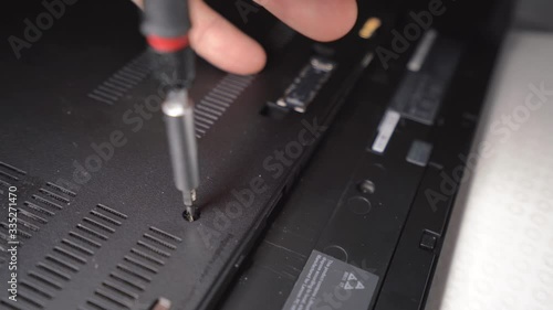 Unscrewing small screw with screwdriver to remove laptop base cover photo