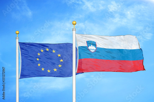 European Union and Slovenia two flags on flagpoles and blue cloudy sky