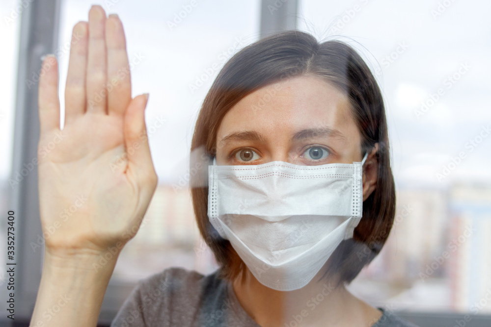 girl in a medical mask behind a glass window on self-isolation during quarantine. girl in a medical mask behind a glass window on self-isolation during quarantine.