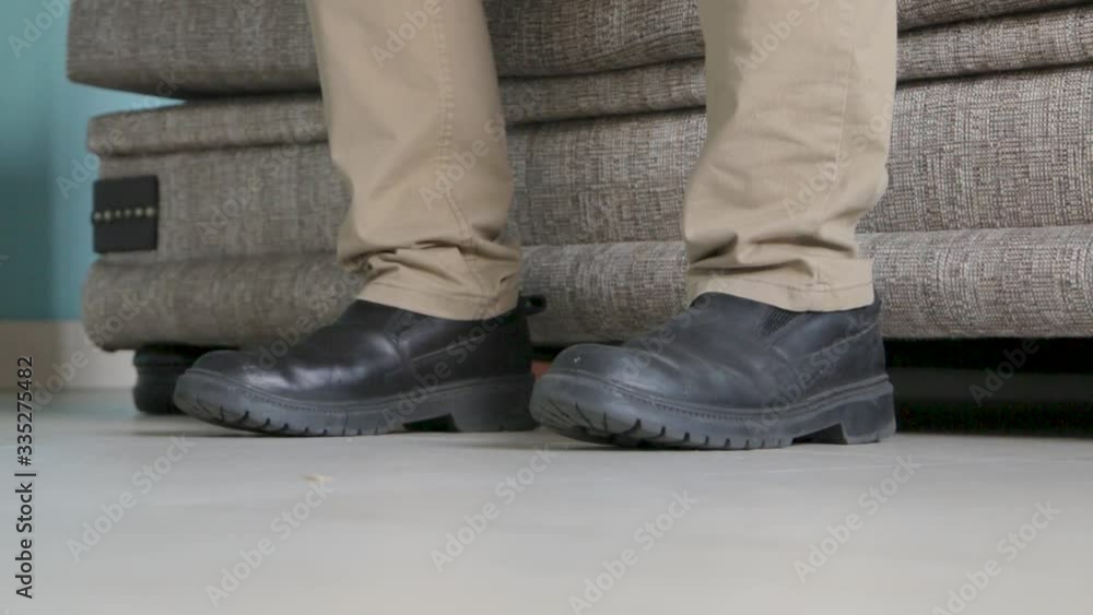 static shot of a man with shoes on gets up from couch and walks off